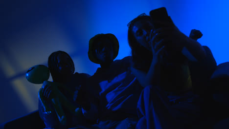 Studio-Shot-Of-Group-Of-Gen-Z-Friends-Sitting-On-Sofa-Posing-For-Selfie-On-Mobile-Phone-At-Night-With-Flashing-Light-2